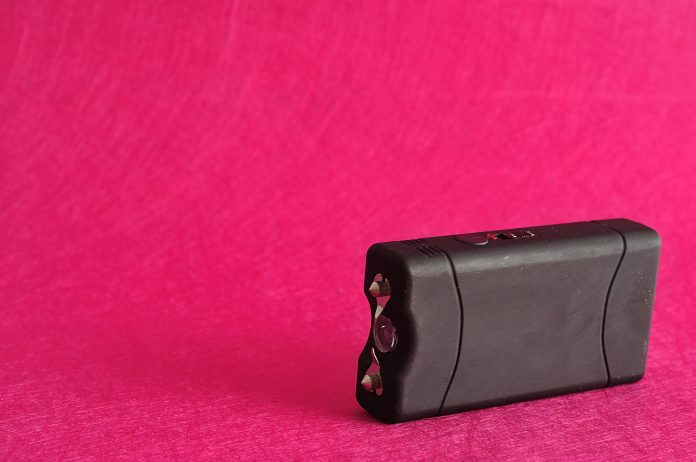 A black taser isolated against a pink background