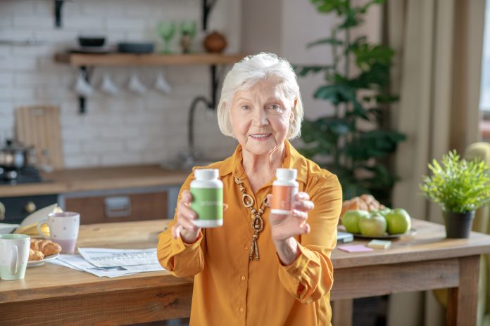 Be healthy. Grey-haired good-looking woman showing two jars with vitamins