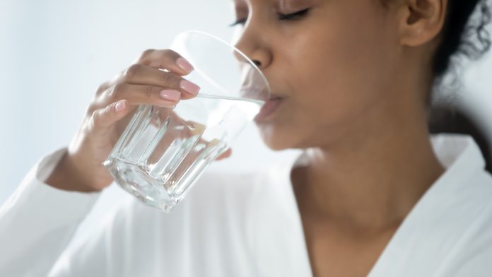 Close up beautiful african woman holding glass drinking a pill with still water. Minerals and vitamins for female, dietary supplement, reducing of thirst, body water balance healthy lifestyle concept