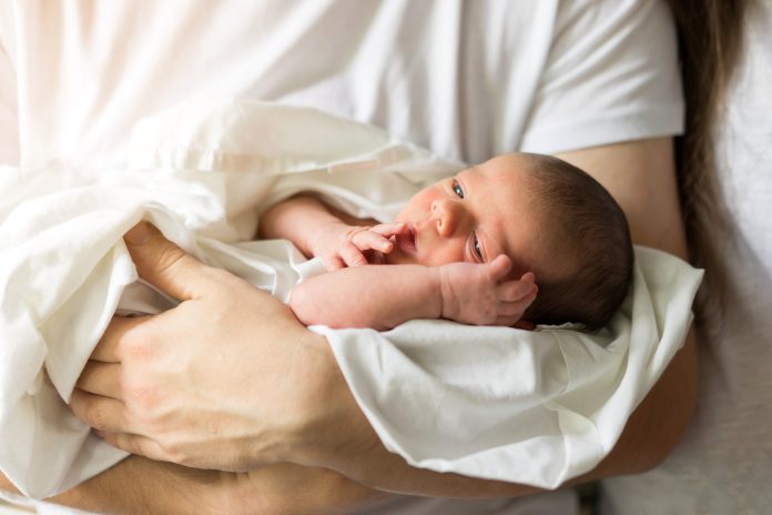 Un padre sostiene en sus manos a su hijo recién nacido desnudo y con un pañal blanco. Nueva vida familiar