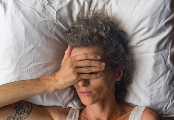 Primer plano en ángulo alto de una mujer de mediana edad durmiendo sobre la almohada con la mano sobre los ojos (enfoque selectivo)