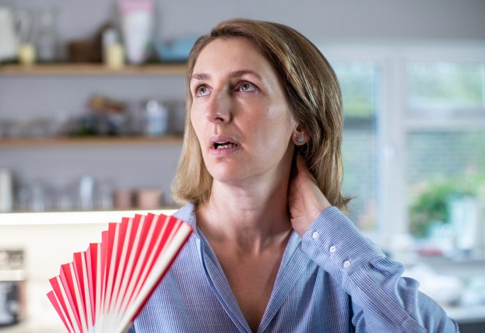 Mujer madura que experimenta sofocos por la menopausia usando un ventilador