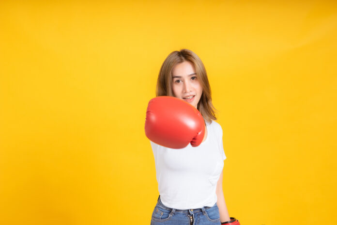 Portrait happy young asian woman with boxing glove punching hit or self defend in white t-shirt, Yellow background isolated studio shot and copy space.