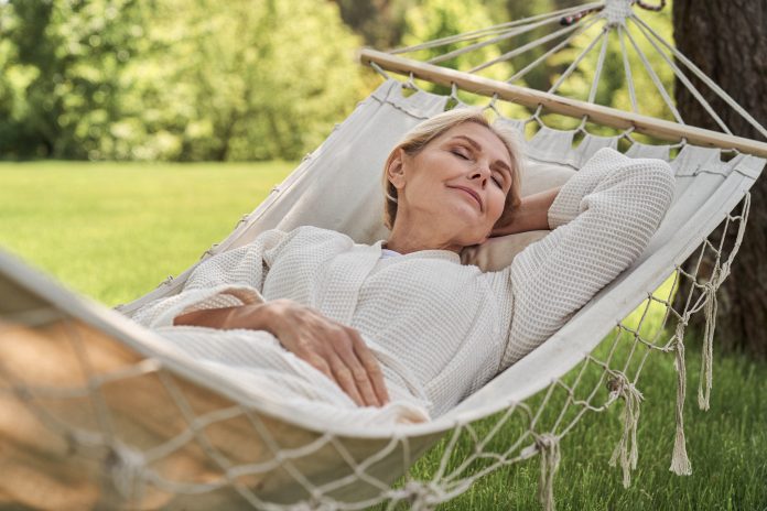 Smiling beautiful woman is having rest in green yard in open air on sunny warm day