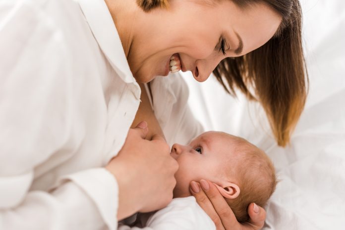 Joven madre sonriente con camiseta blanca amamantando a su bebé