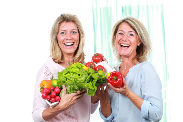 Two happy middle age woman with different vegetables and salad