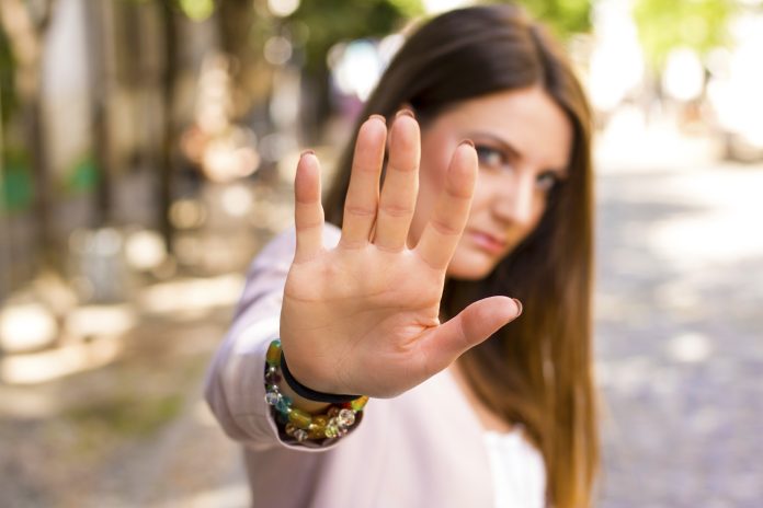 Frau mit ausgestreckter Hand, die signalisiert, dass sie anhalten soll. Negative menschliche Emotion. Körpersprache. Den Abstand halten
