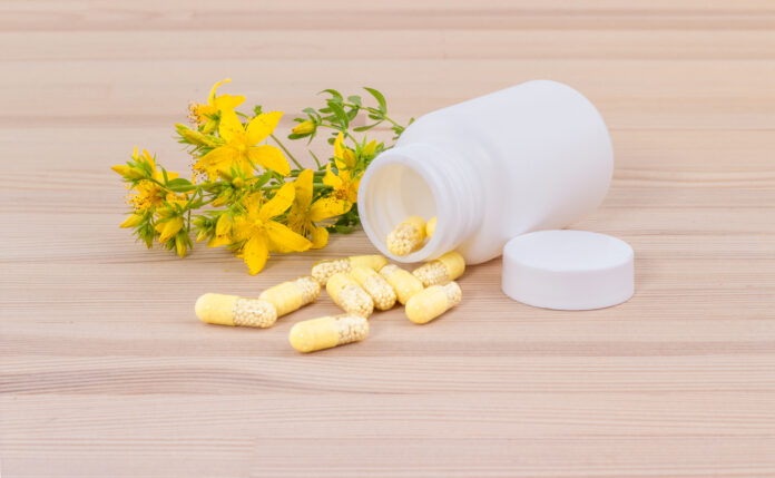 blooming St. John's wort and white container with medicines  on wooden ground