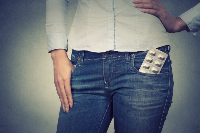 Closeup cropped image of a woman with pills in her pocket on gray background