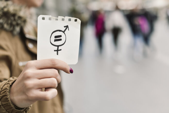 closeup of a young caucasian woman in the street showing a piece of paper with a symbol for gender equality drawn in it