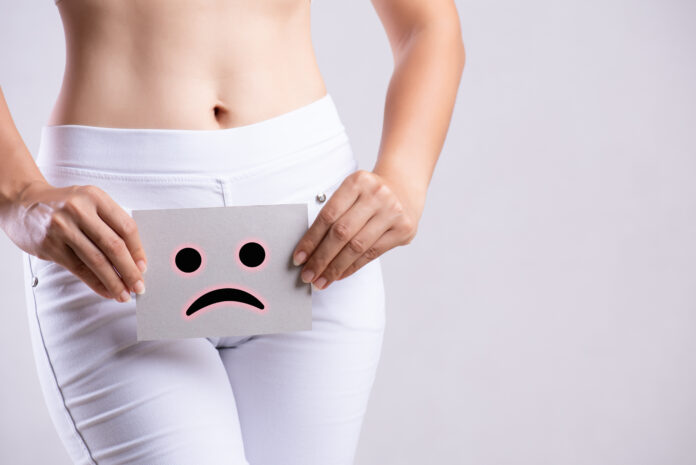 Closeup young woman holding paper with sad smiley face or unhappy near her crotch lower abdomen. Medical or gynecological problems, healthcare concept.