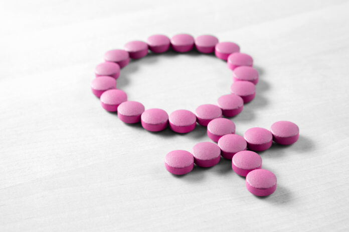 Salud femenina. Símbolo de género hecho con píldoras o pastillas rojas de color rosa sobre una mesa de madera