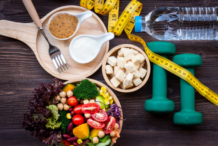 Frischer Gemüsesalat und gesunde Lebensmittel für Sportgeräte für Frauen Diät Abnehmen mit Maßnahme Hahn für die Gewichtsabnahme auf Holz Hintergrund. Gesunder Sport Konzept