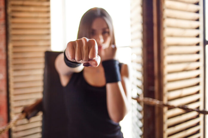 Girl fighter in the gym makes a blow to the camera, fist in focus