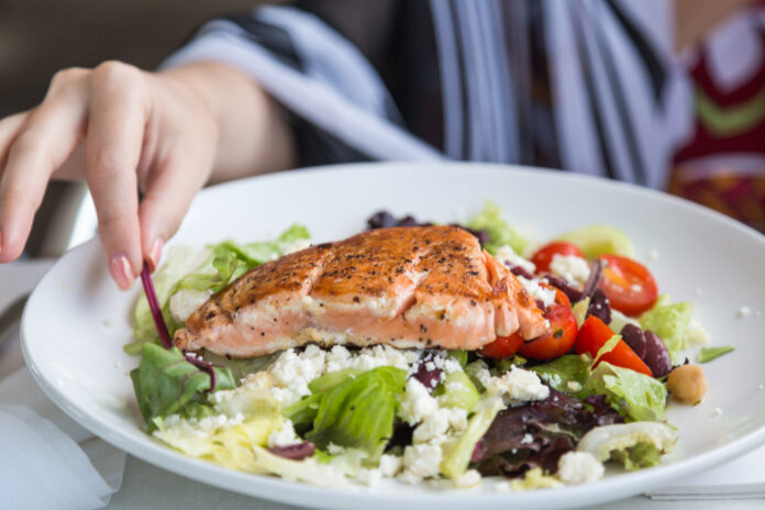Grilled salmon salad with tomato, feta cheese, lettuce and so on and hand approaching.