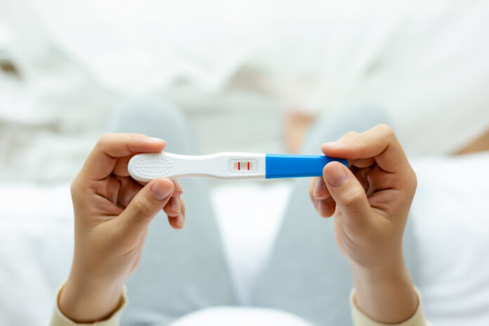 Happy pregnant woman holding pregnancy test, examine positive test, young lady has baby or fetus in belly. Young Mother waiting newborn baby prenatal, pregnancy, motherhood, expecting concept