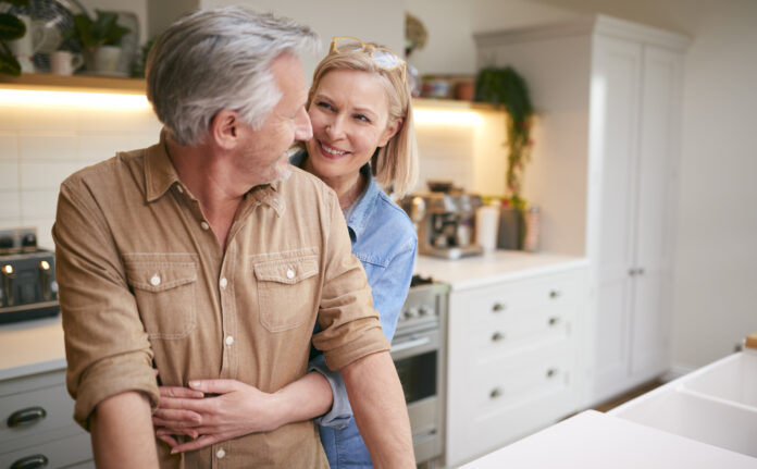 Loving Mature Couple Hugging As They Stand By Counter In Kitchen At Home