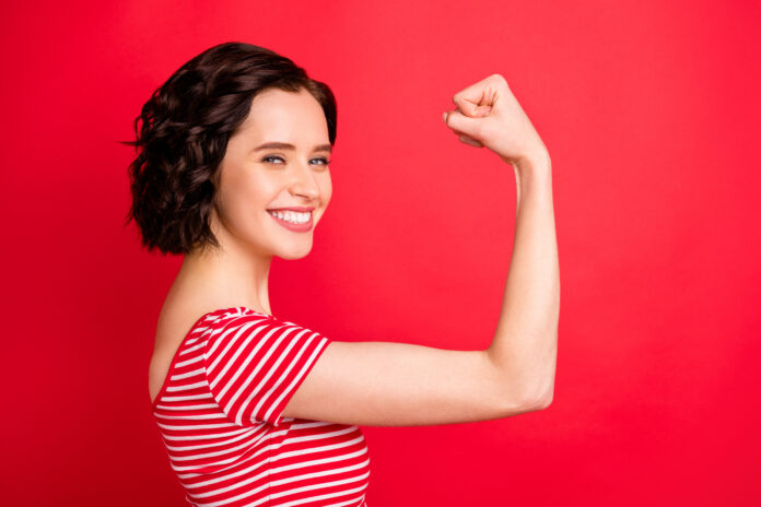 Photo of rejoicing wavy, curly woman after having done two pushups while isolated with red background