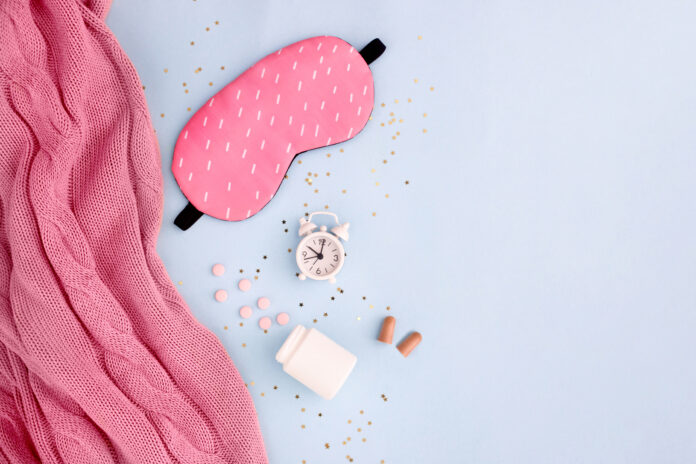 Pills, bottle, sleeping mask, blanket and white alarm clock on blue pastel background. Concept Insomnia, sleep problems, time to take pills and treatment. Top view, flat lay, copy space.