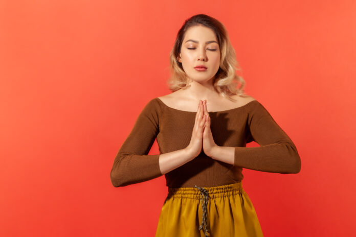 Porträt der ruhigen blonde Frau stehen, nahm die Hände zusammen, beten oder machen Gleichgewicht mit Yoga-Training und geschlossenen Augen. Meditation und konzentriert ihren Geist. Indoor isoliert auf rotem Hintergrund
