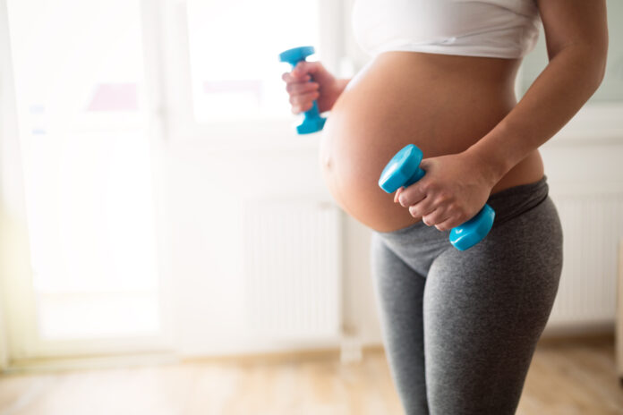 Pregnant woman training with dumbbells to stay active