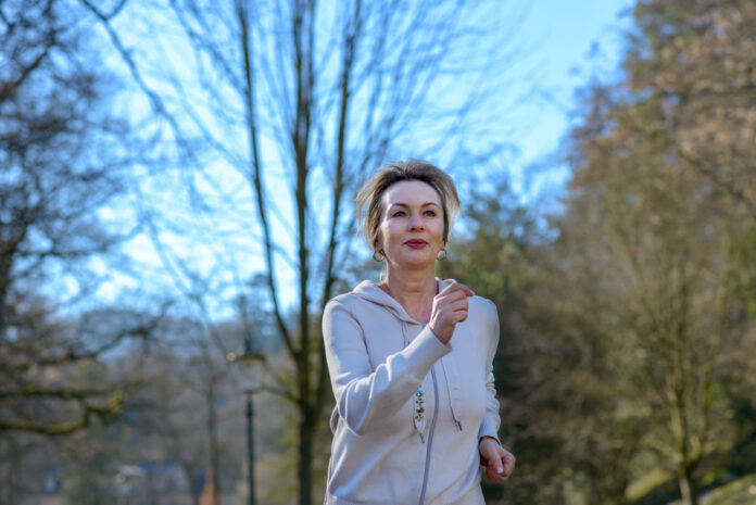 Smiling healthy happy fit senior woman jogging in the park along a tree-lined avenue in a low angle view