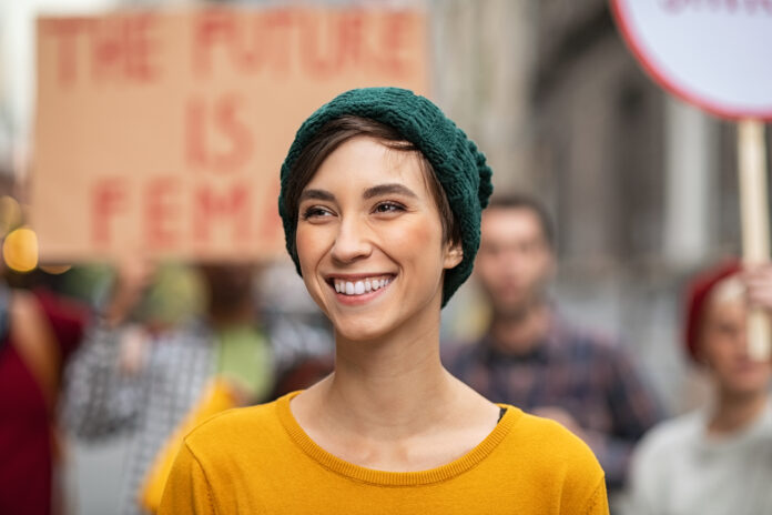 Smiling latin woman in march to protest on equality rights. Happy young woman empowerment strike on street looking away. Portrait of confident casual girl in march fighting for freedom.