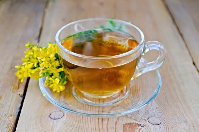 Tee in einer Glastasse, frische Blumen tutsan gegen ein Holzbrett