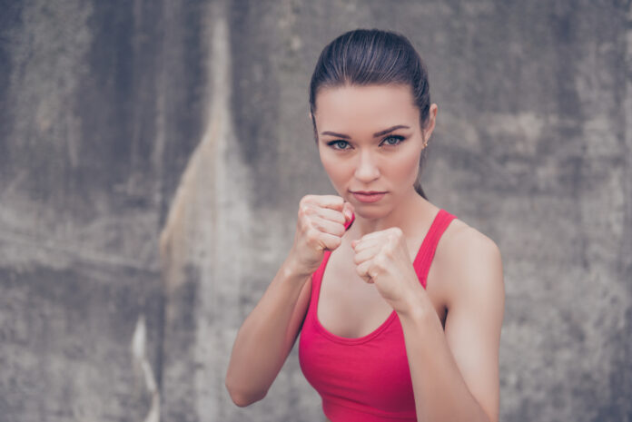 Frau Macht, Selbstverteidigung Konzept. Close up Porträt der attraktiven ernst fit Boxer, bereit für den Kampf, auf Betonwand Hintergrund, tragen rosa modische Sportkleidung