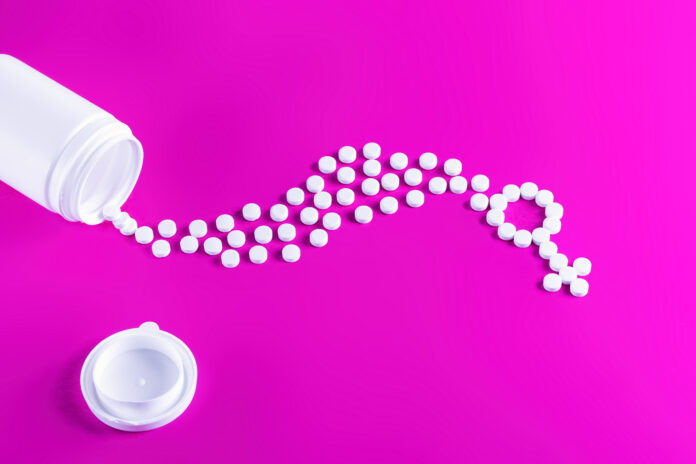 Women's health medical concept. Pills are poured out of a bottle and stacked in a female gender symbol on a pink background.
