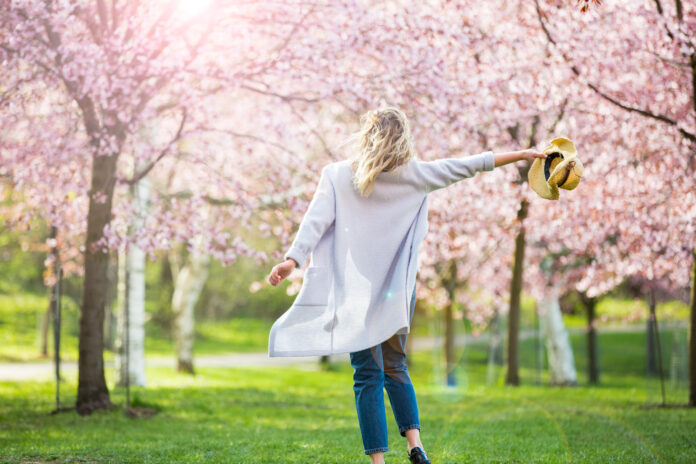 Young woman enjoying the nature in spring. Dancing, running and whirling in beautiful park with cherry trees in bloom. Happiness concept