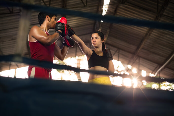 Young woman exercising with trainer at boxe and self defense lesson. Copy space