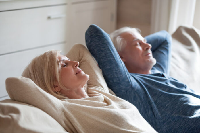 Calm senior mature couple relaxing on soft comfortable sofa having daytime nap together, carefree middle aged old family breathing fresh air enjoying no stress free peaceful weekend resting on couch