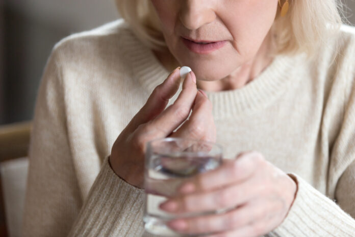 Close up of unhealthy middle aged woman suffers from pain, holding pill and glass of still water feels ill taking medicine, cropped image. Disease prevention and treatment of old mature people concept