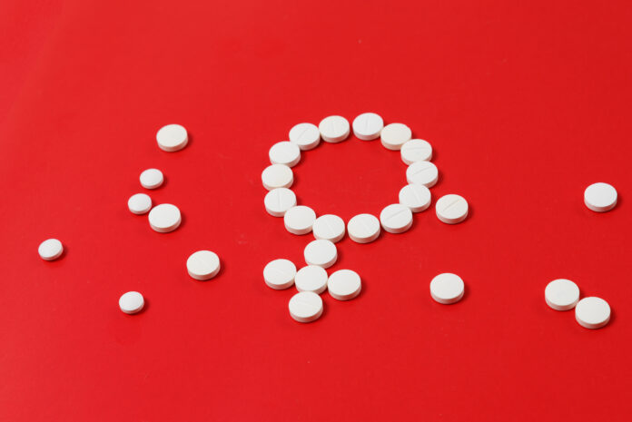 Concept Female health. Gender symbol made from white pills or tablets on red background.