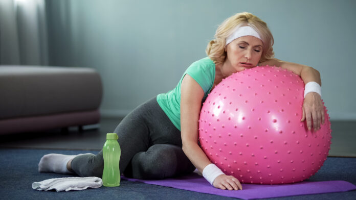 Exhausted mature female lying on fitness ball, relaxing after active workout