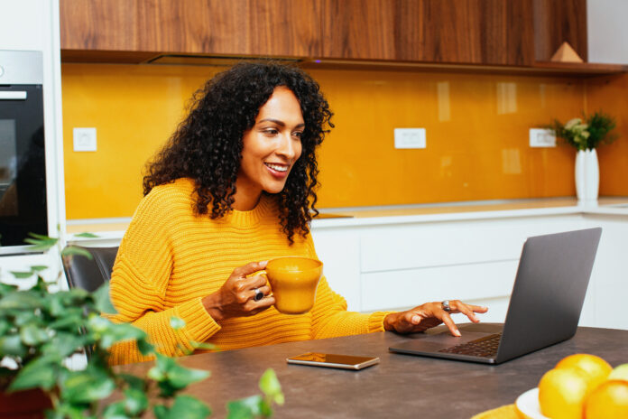 Portrait of a mid woman with black curly hair smiling while using laptop computer in kitchen