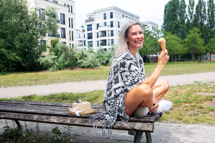 beautiful blond woman sitting on bench in a park eating ice cream
