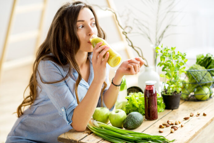 Beautiful woman sitting with healthy green food and drinking smoothie at home. Vegan meal and detox concept