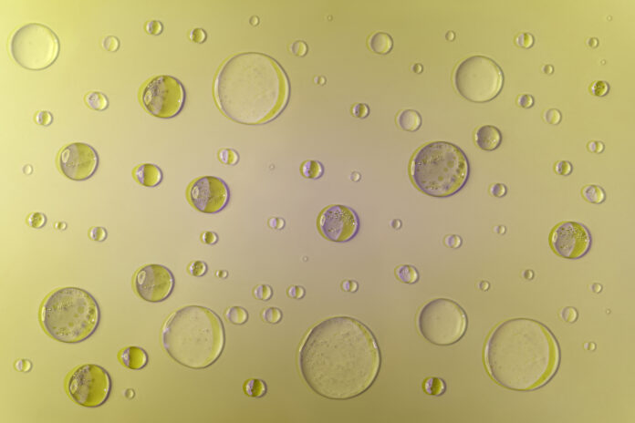 Burbujas de gel y suero con sombras y reflejos morados. Sobre fondo amarillo, vista superior.