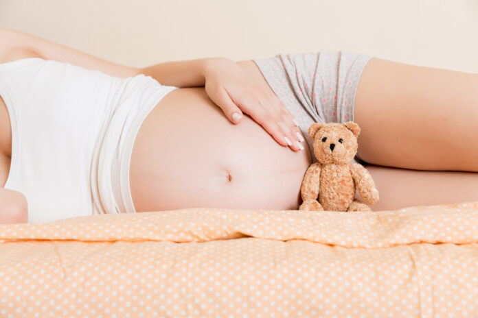 Closeup of pregnant woman with teddy bear lying on bed.