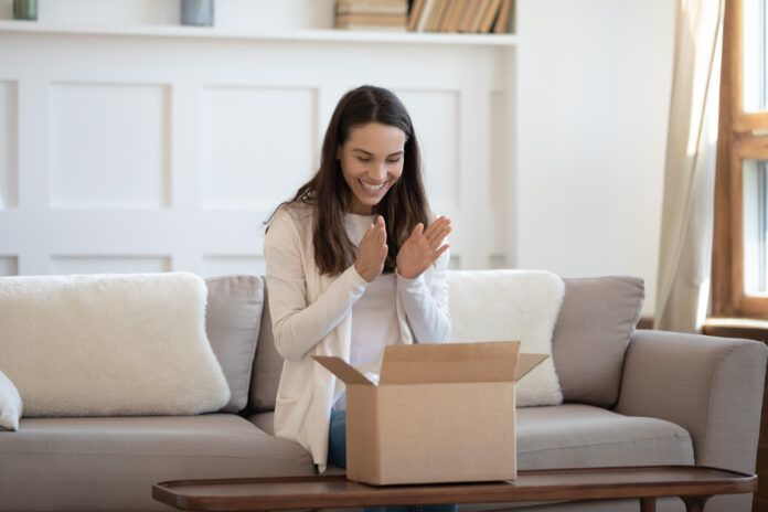 Aufgeregt junge kaukasische Frau sitzen auf Sofa zu Hause fühlen euphorisch unbox Internet-Bestellung-Paket, glücklich Millennial weiblich unpack box Online-Shopping, zufrieden mit guter Qualität Produkt, Lieferung Konzept