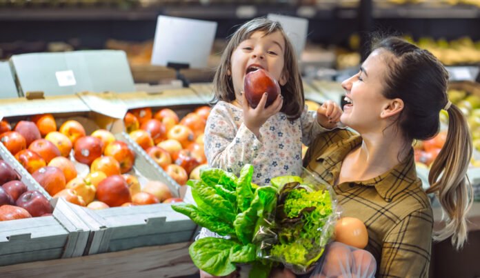 Familia en el supermercado. Hermosa madre joven y su pequeña hija sonriendo y comprando comida. El concepto de alimentación saludable. Cosecha