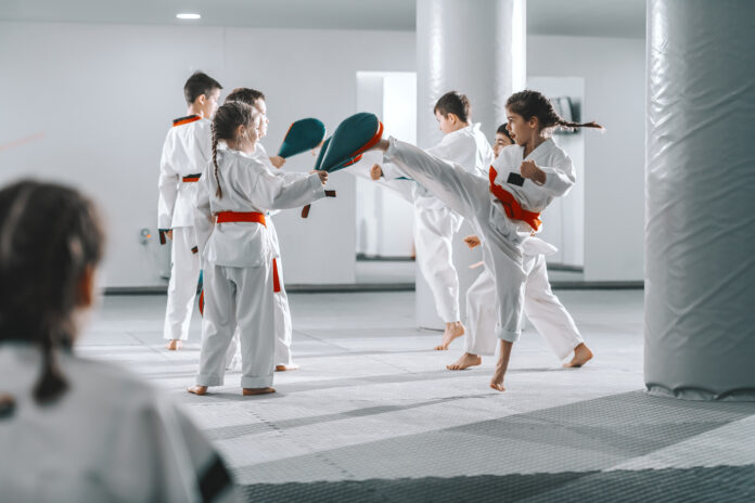 Grupo de niños caucásicos deportistas en doboks teniendo clase de taekwondo en gimnasio blanco.