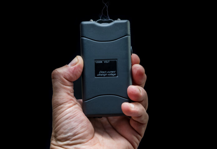 Hand hält einen Elektroschocker vor schwarzem Hintergrund