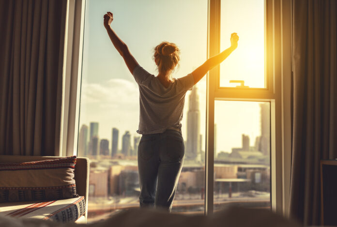 glückliche Frau streckt sich und öffnet die Vorhänge am Fenster am Morgen