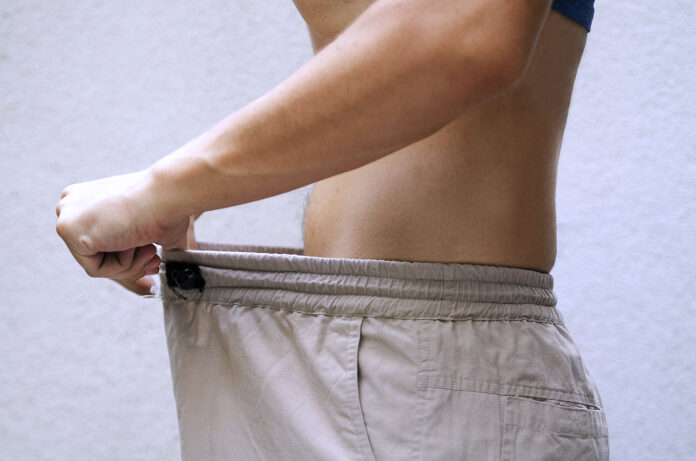 Man efter diet jämför sin midjestorlek på byxor.Slim fit manlig kropp eller genitala problem.