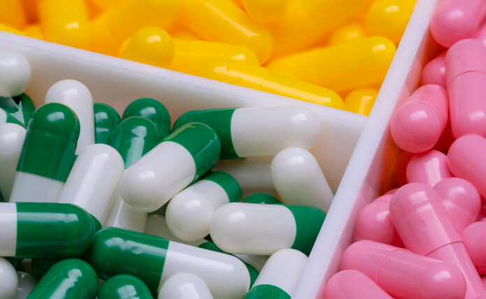 Pink and green-white capsule pills on blur yellow capsule pills in a plastic box. Vitamins and supplements concept. Pharmaceutical industry. Pharmacy products in drug tray. Health insurance background