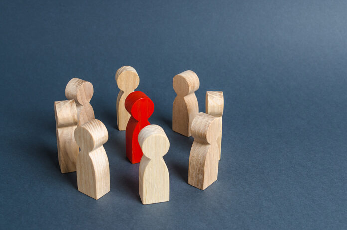 Figura humana roja rodeada de un círculo de personas. Jefe y liderazgo. Cooperación y trabajo en equipo. Paria, oponente odiado, criminal. Condena. Discriminación y violencia.