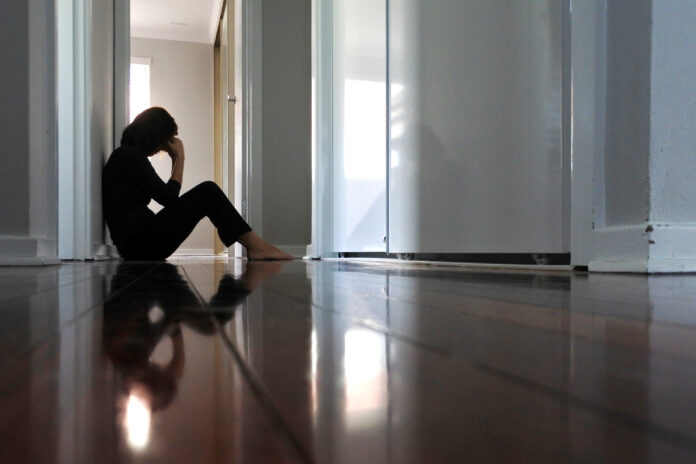 Sad adult woman sitting on dark home corridor floor.